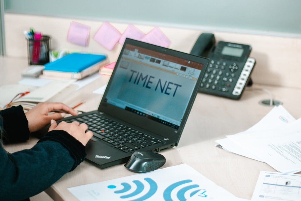 Person using laptop at an office desk in Erbil with phone and documents visible.